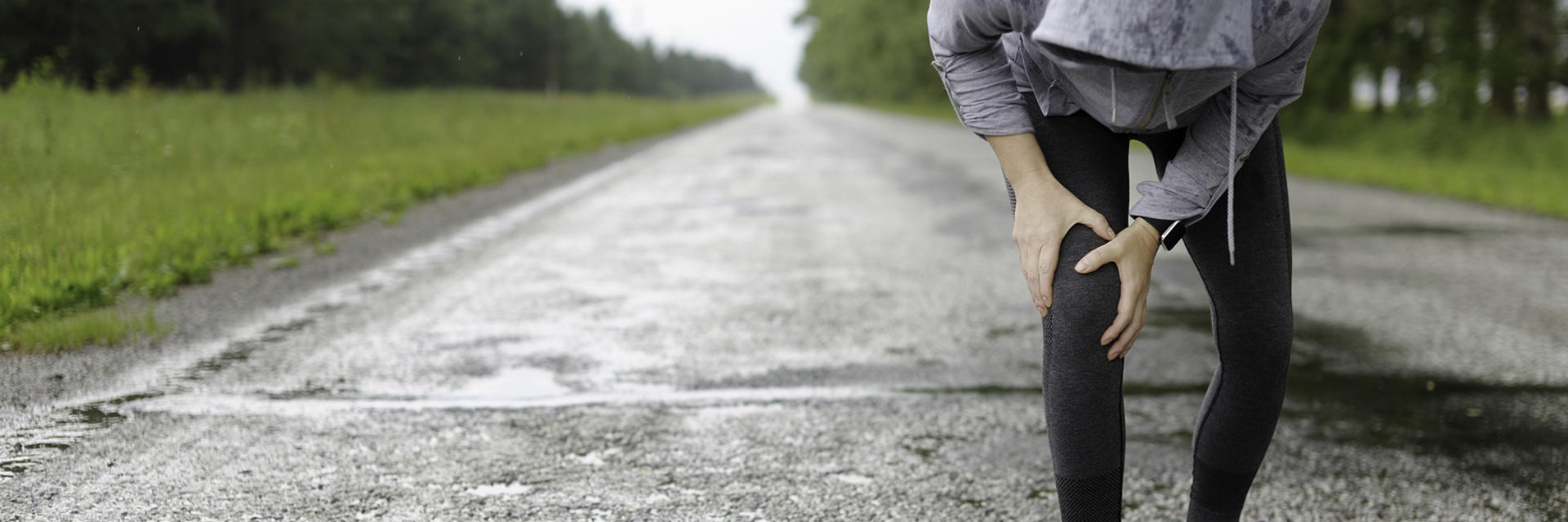 A person running outdoors stopped by pain in the knee area.