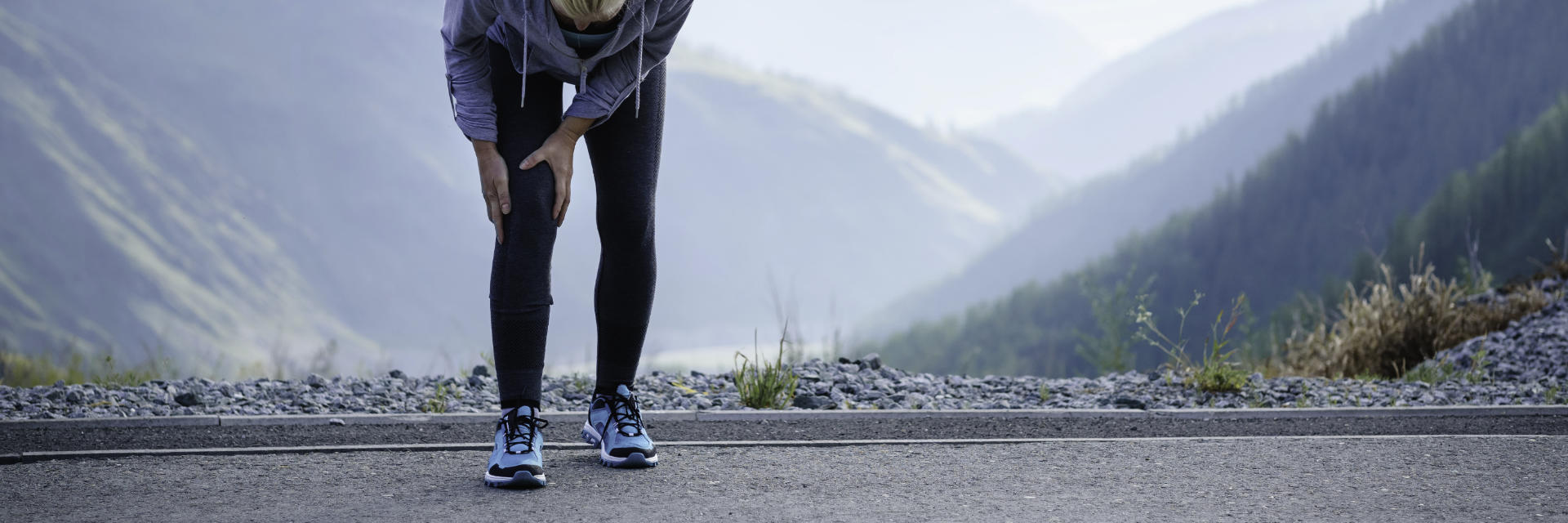 A woman running outdoors stopped by pain in the knee area.