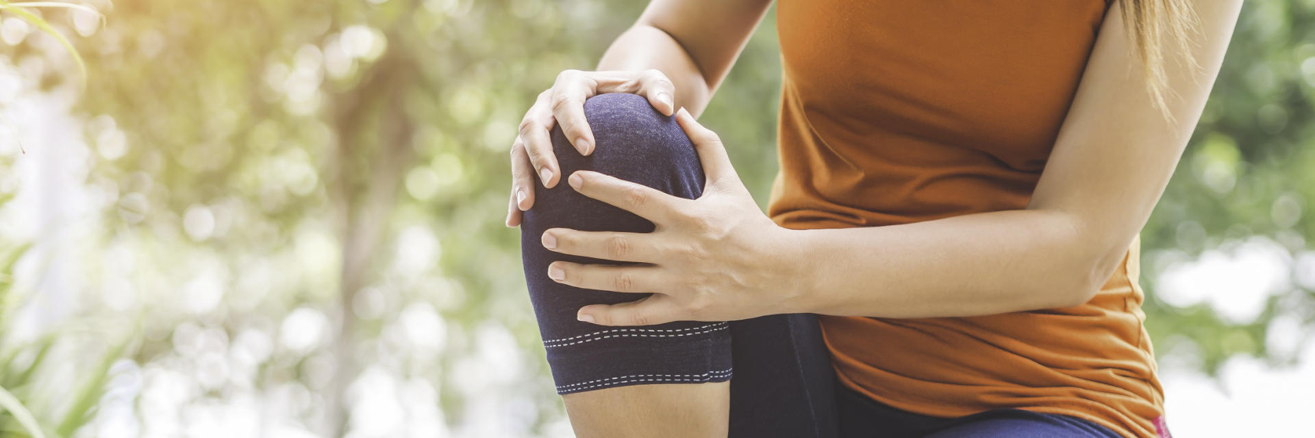 Woman with pain due to injured knee holding it with both hands.