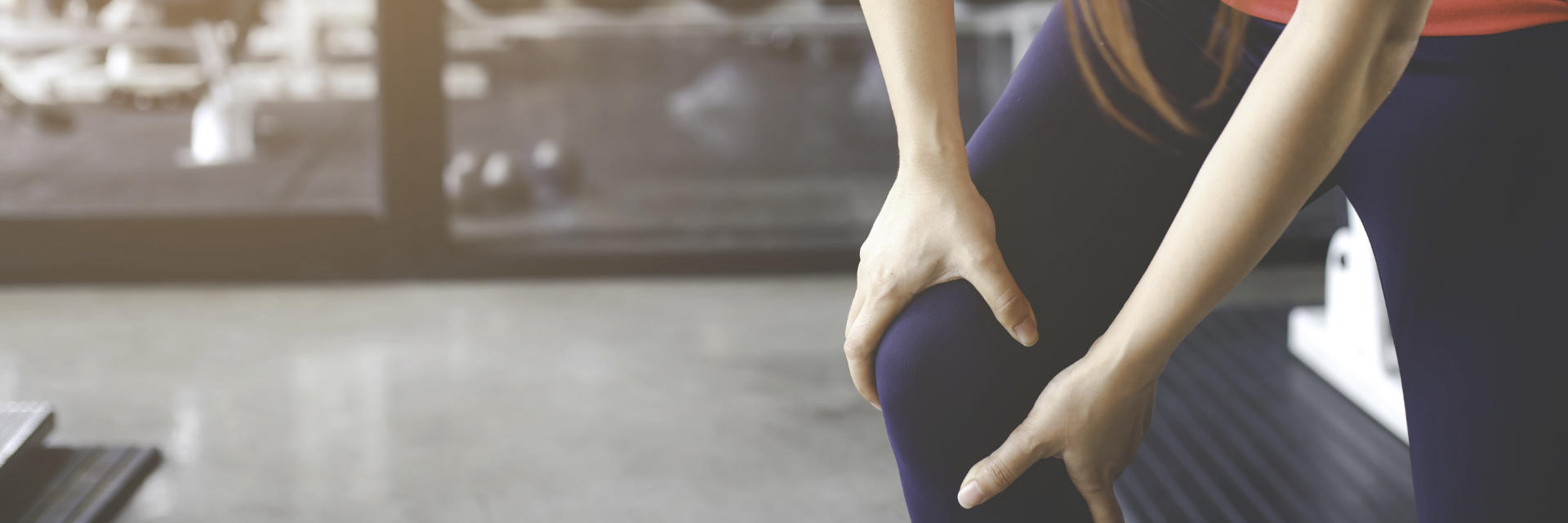 A woman holding her knee in pain due to injury she experienced while working out at the gym.