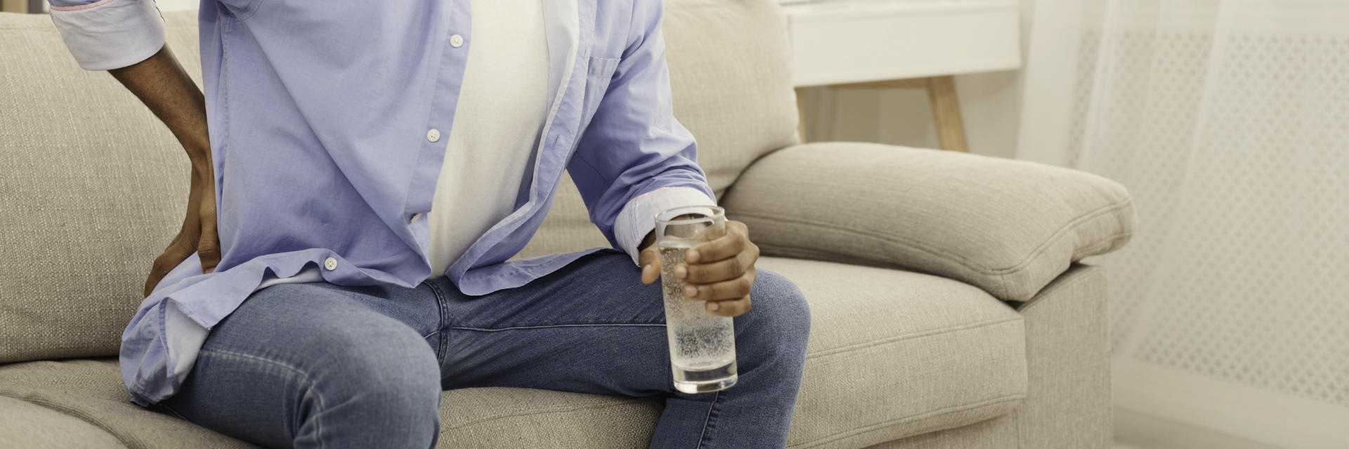 A man with hip pain trying to sit down on the sofa.