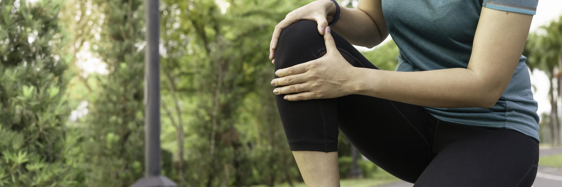 A woman running in the park stopped by pain in the knee area.