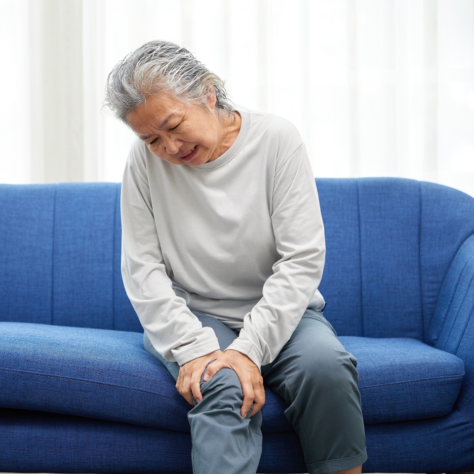 senior woman suffering from knee ache on sofa