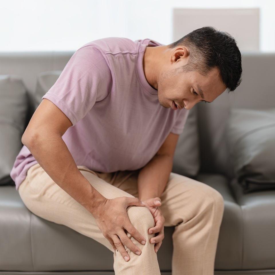 Knee pain sick body health care concept A young man has knee pain, sitting on the sofa at home, touching his leg, feeling pain in his knee.