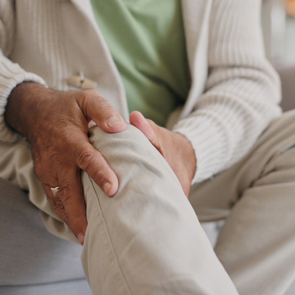 Home, knee pain and senior person with arthritis, osteoporosis and fibromyalgia on sofa. Medical, hands and man with joint massage for relief, muscle tension and accident or injury in retirement