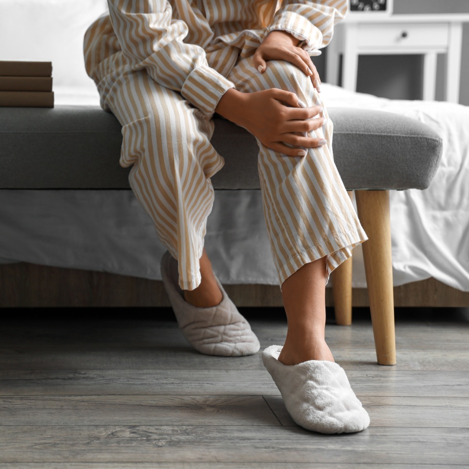 Young woman suffering from knee pain in bedroom
