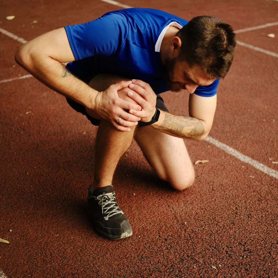 Knee Pain. Sport injury concept. Young man has knee pain during outdoor exercise. Sports running knee injury in male runner on the treadmill near the stadium