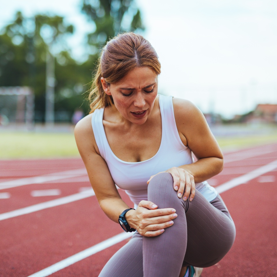 A female athlete experiences knee pain while seated on an outdoor track. The image conveys determination, resilience, and the challenges faced in sports and fitness activities.