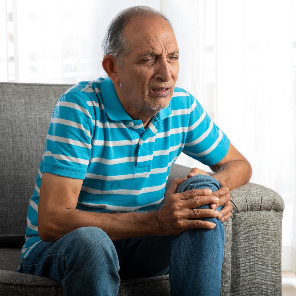 Senior man sitting at home with a knee pain (Health and fitness)