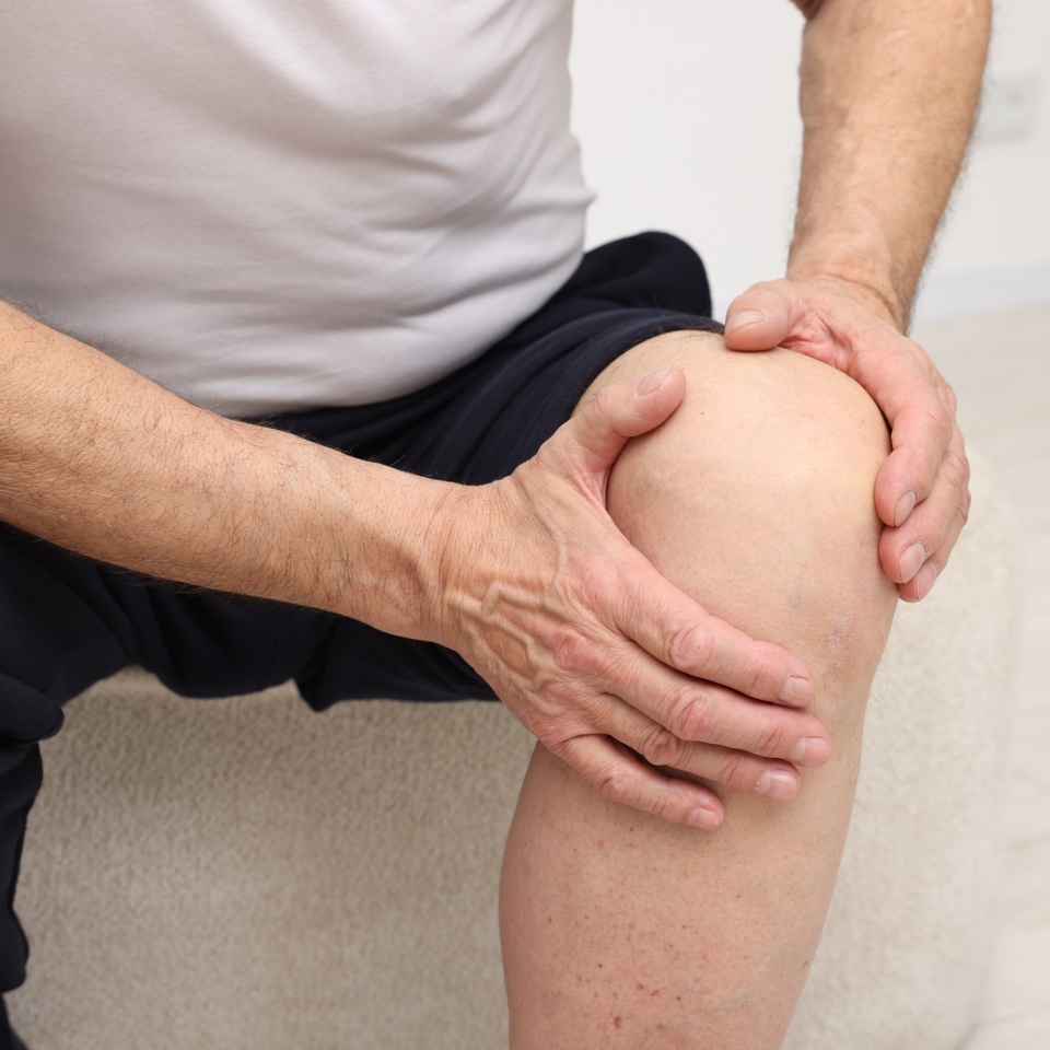 Senior man suffering from knee pain on pouf indoors, closeup
