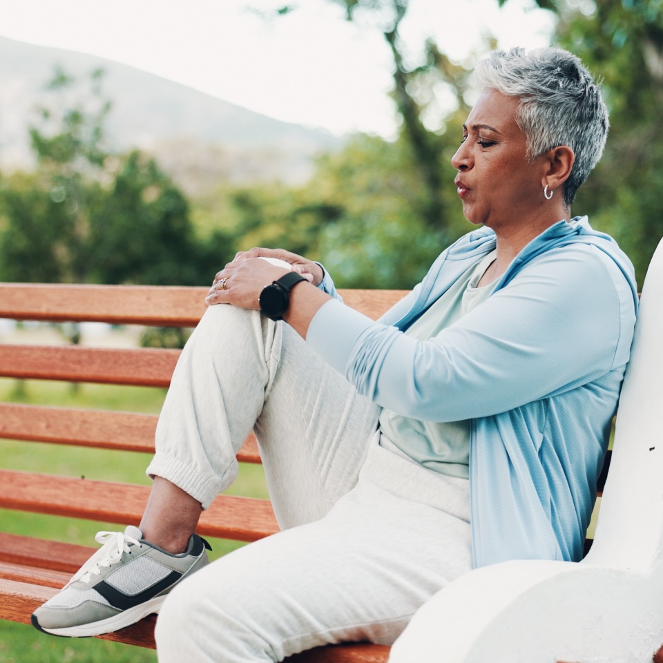 Knee pain, fitness and mature woman in park with injury, muscle strain and inflammation on bench. Nature, sports and senior person with accident for exercise, workout and walking outdoors for health