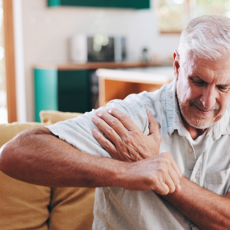 Home, shoulder pain and senior man on sofa, broken and pressure in living room. Pensioner, apartment or mature person on couch, inflammation or joint injury in lounge, stress and bruise with burnout