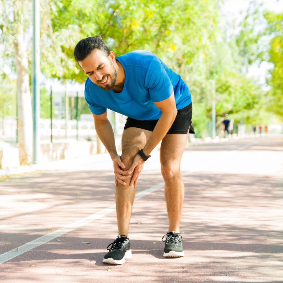Hispanic sportsman feeling a sharp pain in his knee while exercising outdoors on a running track