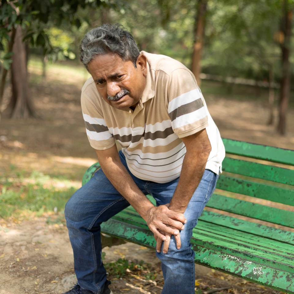 Indian senior man suffering from knee pain at park.