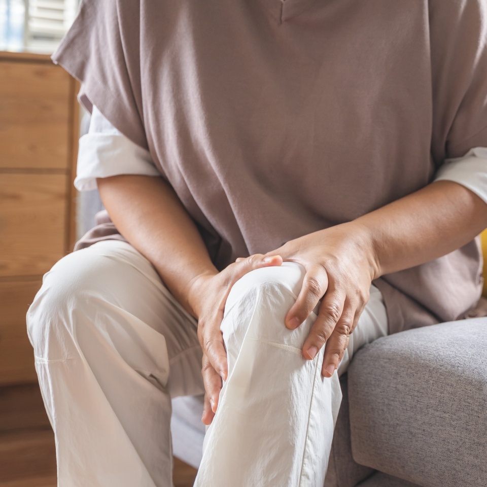 Body arthritis muscles stiff problem, aged woman suffering on leg, pain knee from disease chronic, hand massage rubbing joint injury, mature hurt or sore sitting on sofa at home. Health care people.