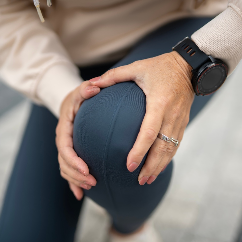 Woman touching her knee in discomfort, experiencing joint pain and injury during or after a physical workout, highlighting common health issues and sports-related problems