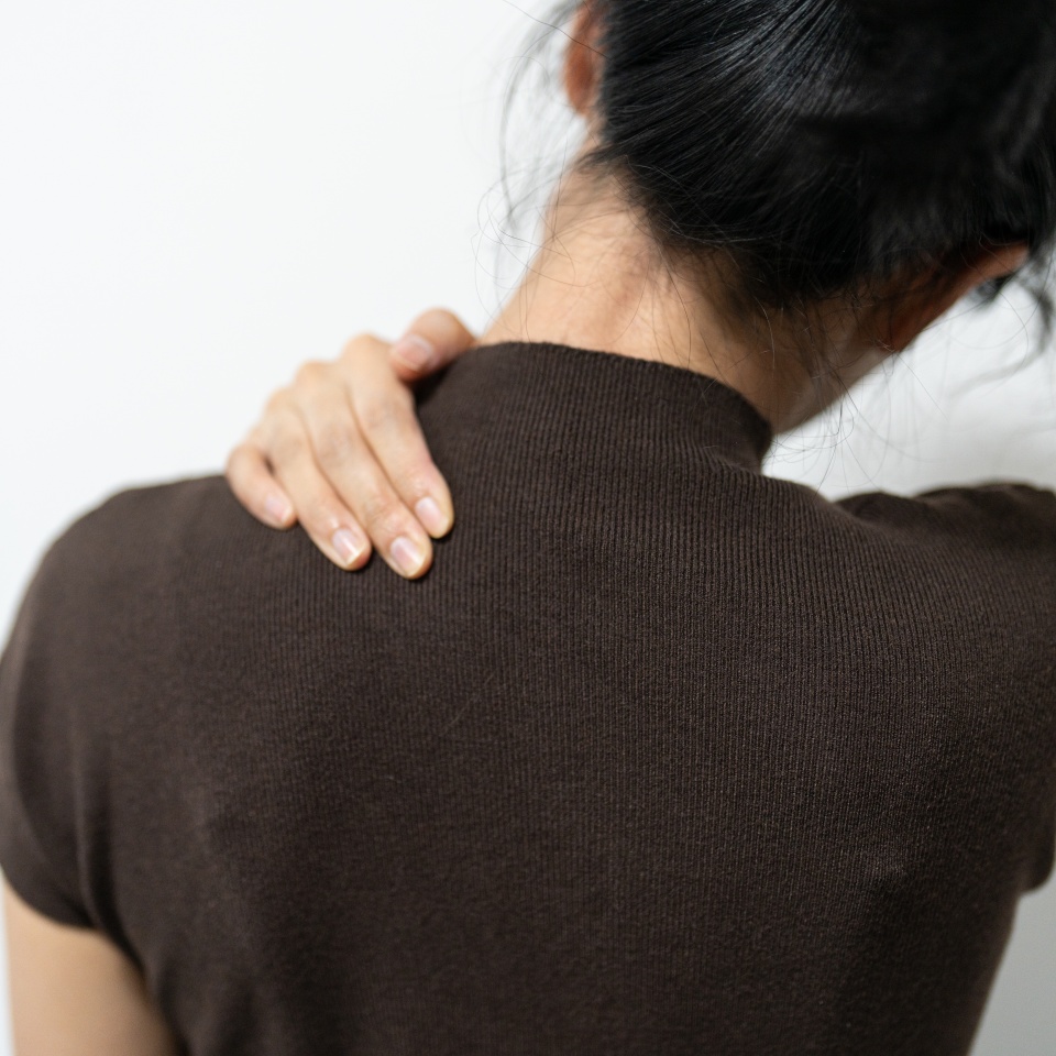 office syndrome in office worker concept. A person with dark hair reaches back to touch their shoulder, expressing discomfort or tension.
